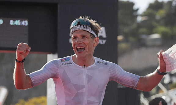Professioneller Triathlet jubelt nach einem erfolgreichen Wettkampf, Symbol für Ehrgeiz und Entschlossenheit bei Hofmann Personal.