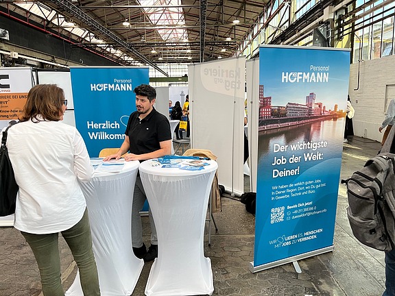 Hofmann Personal Messestand mit Beratungsgespräch an Stehtischen vor blauem Branding