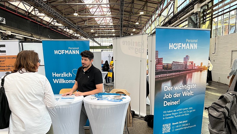 Hofmann Personal Messestand mit Beratungsgespräch an Stehtischen vor blauem Branding