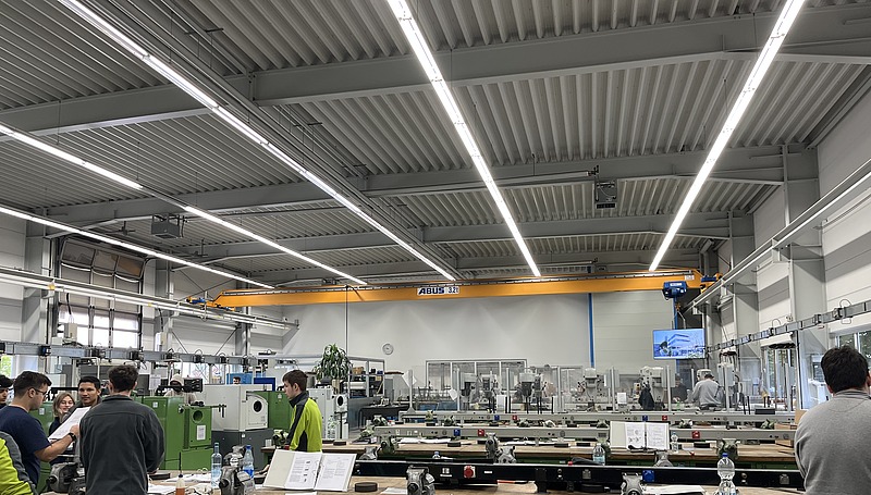 Viele Mitarbeitende arbeiten konzentriert an Maschinen und Werkbänken in heller Umgebung