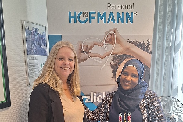 Eine lächelnde Mitarbeiterin von Hofmann Personal, steht neben einer ehemaligen externen Mitarbeiterin, die eine Festanstellung in einem Restaurant erhalten hat.