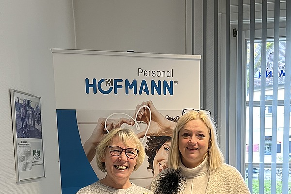 Eine lächelnde Mitarbeiterin, steht neben einer ehemaligen externen Mitarbeiterin, die über die Zeitarbeit bei Hofmann Personal ihren Traumjob gefunden hat.